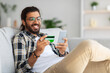 © Prostock-studio - Cheerful indian man with credit card and mobile phone