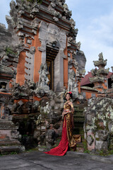 Wall Mural - Beautiful balinese girl in traditional costume with a flower and a crown in her hair, and local temple