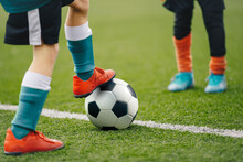 Close Up Image On Soccer Player Legs With Classic Ball. Football Background Of Soccer Field And Players In A Game. Boy In Sports Shoes Kicking Ball.