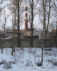 Industrial zone behind a fence on the bank of a frozen river, Monastyrka River, St. Petersburg, Russia, December 2021