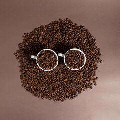 two cups of coffee on a pile of coffee beans on a brown background.