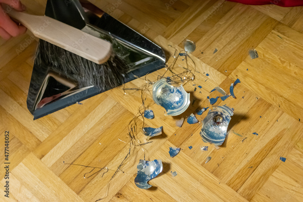 Broken Christmas balls on ground were destroyed by children on Holy Eve during Christmas tree decoration with the family and have to be sweep up with sweeping broom to clean and ornate