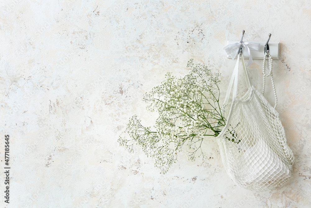 String bag with gypsophila flowers hanging on light wall