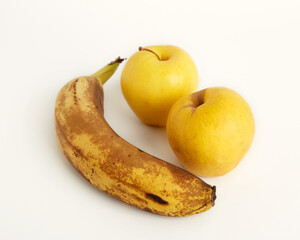 Wall Mural - Darkened banana and flabby yellow apples isolated on white background. Ugly food concept. View from above