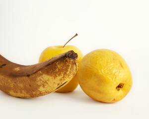 Wall Mural - Shriveled yellow apples and overripe banana isolated on a white background. Ugly food concept. Selective focus