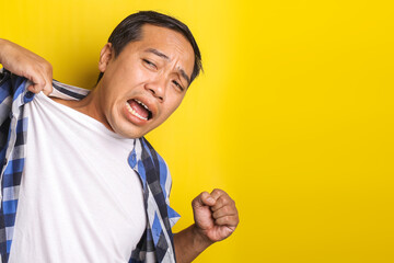 Close-up portrait of asian man with expression of suffering, pain, shirt collar being pulled with copy space isolated on yellow background