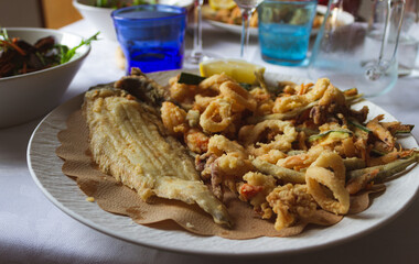 White dish with fried fish and vegetables on the restaurant table.