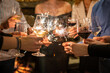 © Miljan Živković - Close up on hands of group of people holding glasses of wine and sparkles while toasting and celebrating indoor focus on sparks birthday or new year celebration concept