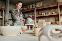 Young Woman Using Stick To Make Little Details On The Clay Sculpture While Working In The Studio