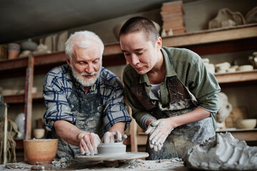 Wall Mural - Senior man showing the woman how to make form of vase from clay on pottery wheel in studio