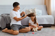 © sementsova321 - Indoor shot of attractive man wearing white t shirt sitting on floor and making hairstyle for his cute little daughter, taking care of his female child, spending pleasant time together.