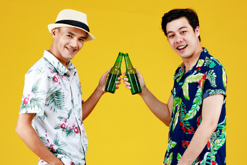 Two young Asian guys cheer with alcoholic drink bottles with smile to celebrate happy friendship at tropical beach party