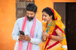 Traditional Indian rural farmer couple using smart phone to make online payment , shopping on internet with cellphone secure banking service system concept.