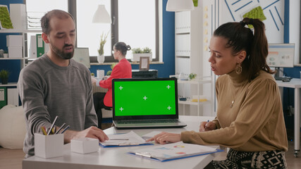 Team of workers having laptop with green screen on desk. Man and woman doing teamwork and using mockup template with chroma key and isolated blank background. Chroma-key copy space