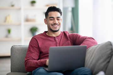 Wall Mural - Positive arab guy surfing on social media, using laptop