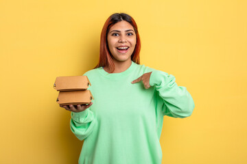 hispanic woman feeling happy and pointing to self with an excited. take away burgers concept