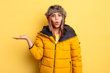 Hispanic Woman Looking Surprised And Shocked, With Jaw Dropped Holding An Object. Winter Concept