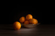 Kompozycja z pomarańczami w ceramicznym naczyniu. Owoce na ciemnym tle