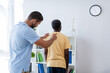 © LIGHTFIELD STUDIOS - doctor examining back of mature african american man in rehabilitation center