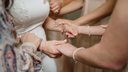 Wall Mural - Cropped photo of Bridesmaids holding hands of the bride Support and love concept Morning preparations of the bride close up Bride in white lace dress 