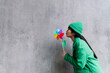 © VISTA by Westend61 - Woman blowing multi colored pinwheel toy at gray wall