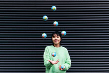 Woman Juggling Globes In Front Of Black Wall