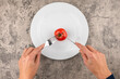 Ein Teller mit einer Tomate die mit Besteck gegessen wird. Konzept Ernährung und Diät bei Übergewicht, gesunde Ernährung