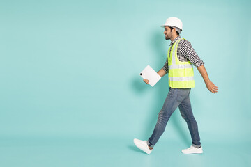 Full length portrait of young professional heavy industry engineer or worker walking and holding tablet Computer isolated on green background, Side view