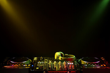 Modern DJ controller and headphones under beams of light on black background