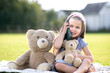 © bilanol - Pretty little child girl sitting in summer park with her teddy bear toy talking on mobile phone smiling happily outdoors in summer.