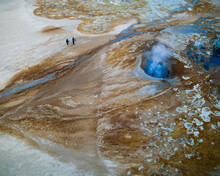 Aerial View Of Two Persons Walking Near A Colourful Mineral Hot Springs In North Iceland.