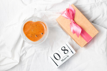 Gift with a pink bow and coffee in a double glass cup with a calendar with the date of March 8 on a white sheet. Breakfast with a present for world Women's Day.