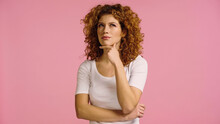 Thoughtful Redhead Woman Standing With Hand Near Face While Looking Away Isolated On Pink
