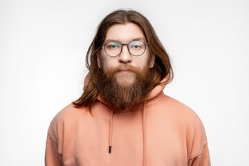 Wall Mural - Scandinavian handsome serious man with glasses and face hair isolated on gray background in orange sweatshirt. Calm nordic guy with long ginger hair and beard