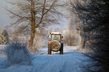 Fototapeta  - Traktor na zimowej polnej drodze z balotem siana