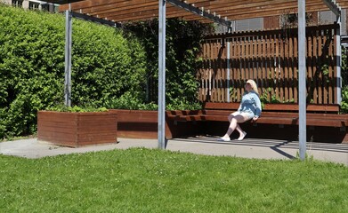 White young woman sitting on a bench in the patio architecture for relaxation during sunny and summer season cooling down in the shadow from the heat wave