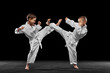 Two little kids, boys, taekwondo athletes training together isolated over dark background. Concept of sport, education, skills