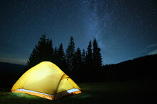 Brightly Illuminated Camping Tent Glowing On Campsite In Dark Mountains Under Night Stars Covered Sky. Active Lifestyle And Traveling Concept