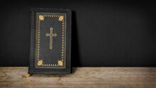 Church Faith Christian Background - Old Holy Bible With Golden Cross On Old Rustic Vintage Wooden Table And Black Wall