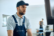 © Drazen - Auto repairman works on desktop PC at car workshop.