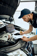 © Drazen - Young repairman takes notes while running diagnostic of car engine in workshop.