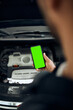 © Drazen - Close-up of mechanic uses smartphone during engine maintenance in workshop.