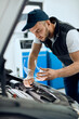 © Drazen - Young mechanic examines car engine at auto repair shop.