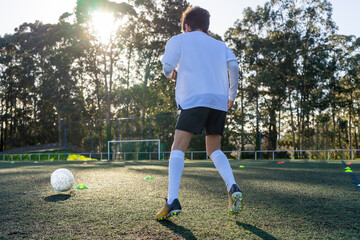 Child with his back to a soccer practice on a sunny day on an artificial turf field. Colored cones demarcating the practice to improve the use of the ball. Concept of sport for children. High quality