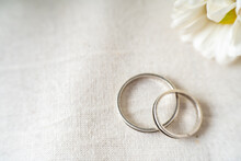 Close-up Of A Pair Of Wedding Or Engagement Rings With An Out Of Focus Background Of Beautiful Violet And White Flowers And A Large Copy Space.