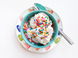 vanilla ice cream with rainbow sprinkles in turquoise bowl on white background