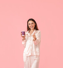 Sticker - Beautiful woman in pajamas and with cup of coffee showing thumb-up on color background