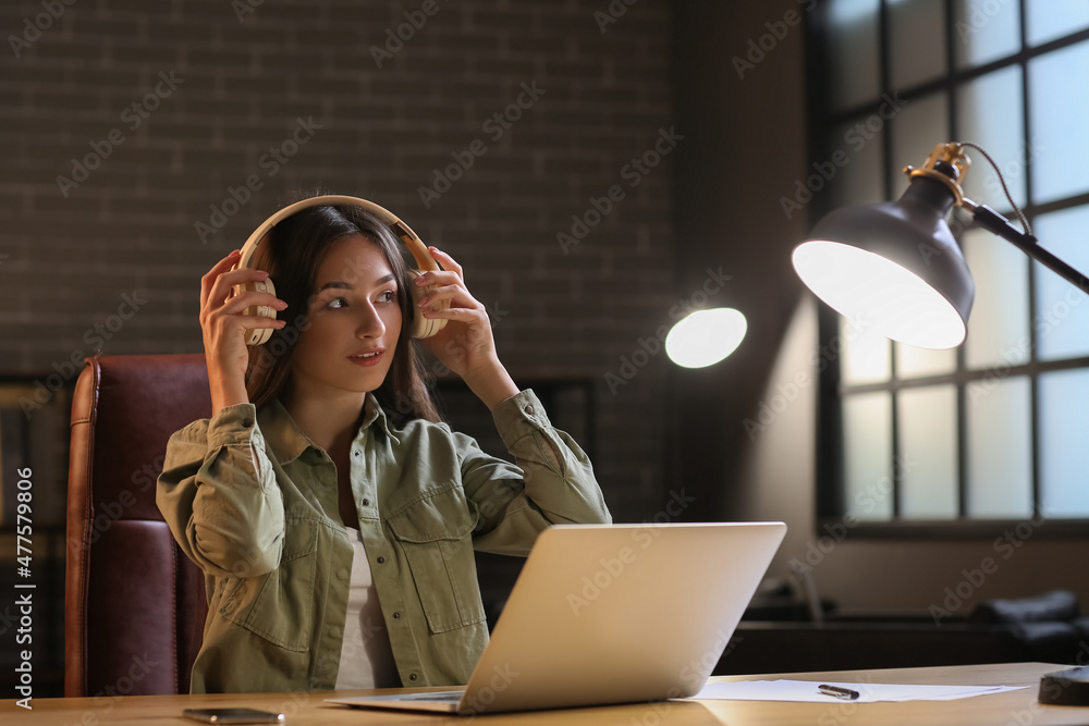 Pretty young woman with laptop listening to music at home in evening