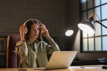 Wall Mural - Pretty young woman with laptop listening to music at home in evening