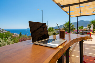 Open laptop with black screen on wooden table work space outdoors with amazing view on the ocean. Laptop on sea view backdrop. Working with view. Home office. Work remote